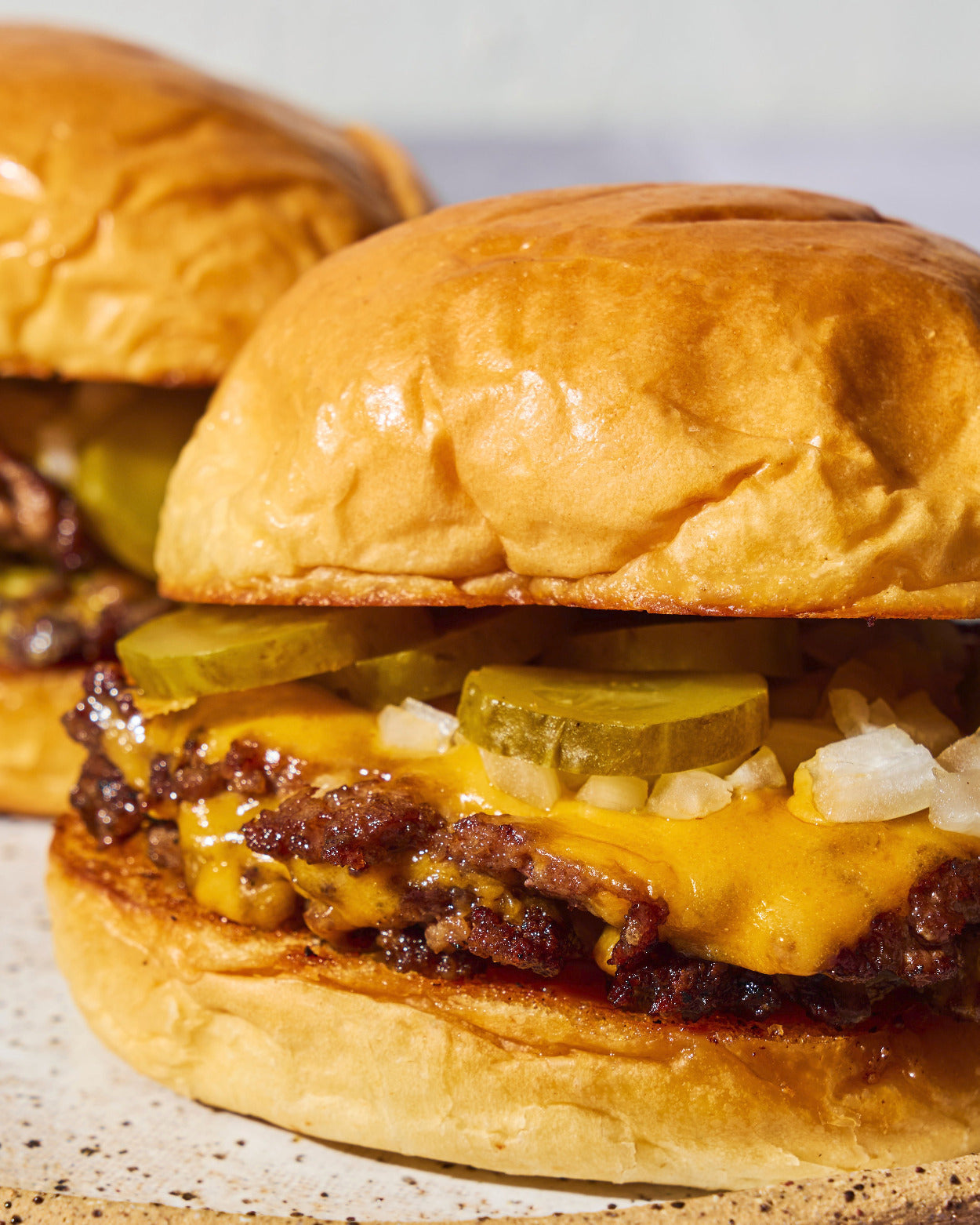 Close-up of a CDH double smash burger recipe with crispy caramelised patties, melted cheese, pickles and diced onion on a toasted brioche bun