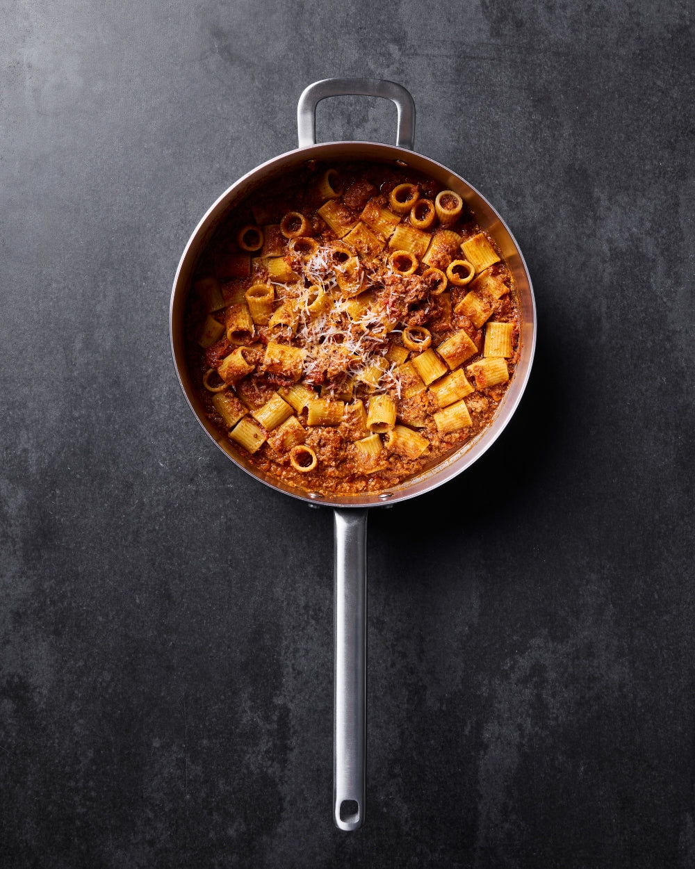 Saute pan with rigatoni pasta and meat sauce on dark kitchen countertop