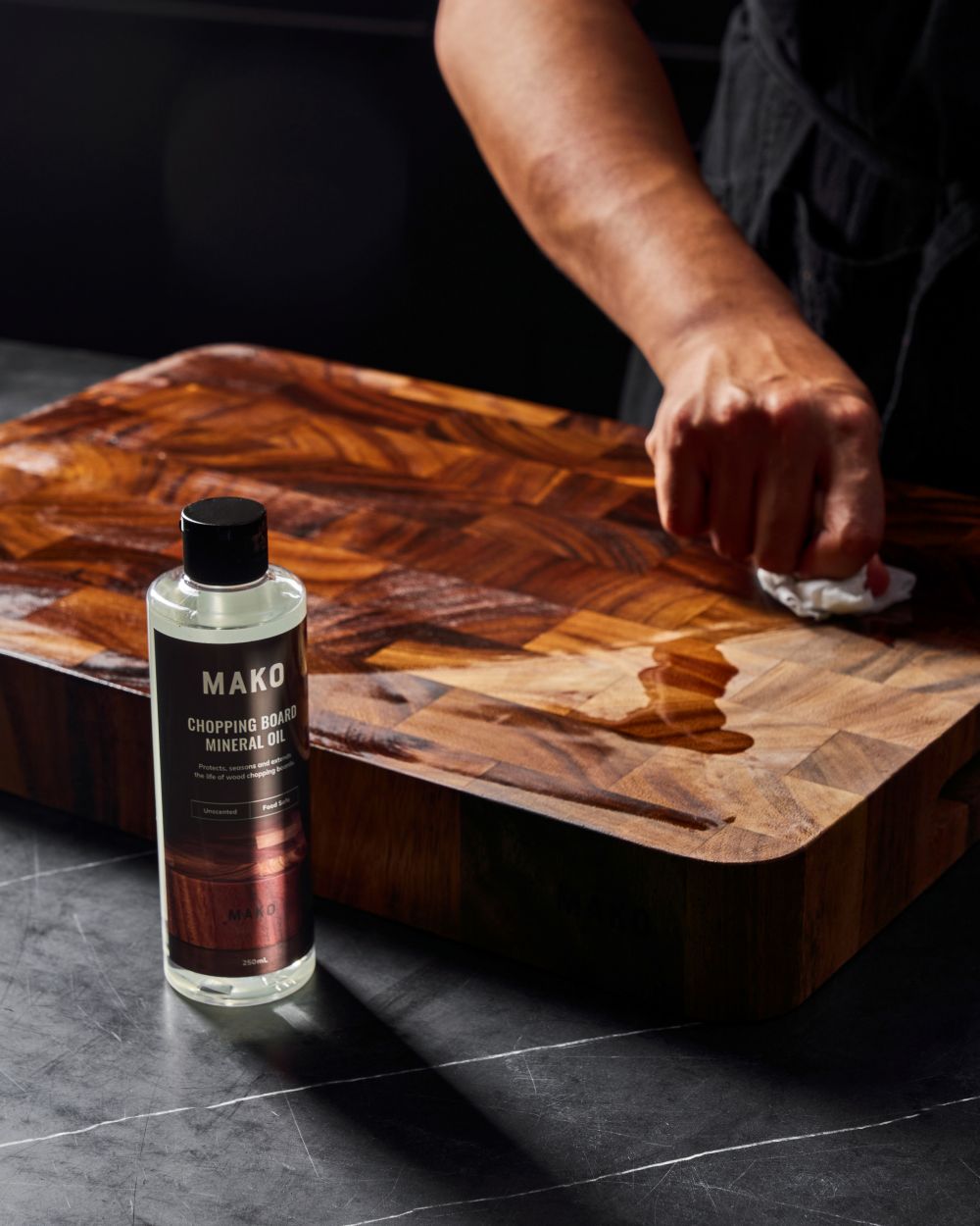 MAKO Chopping Board Mineral Oil in use on the MAKO Butchers Block. Rubbing oil on board on black kitchen bench top