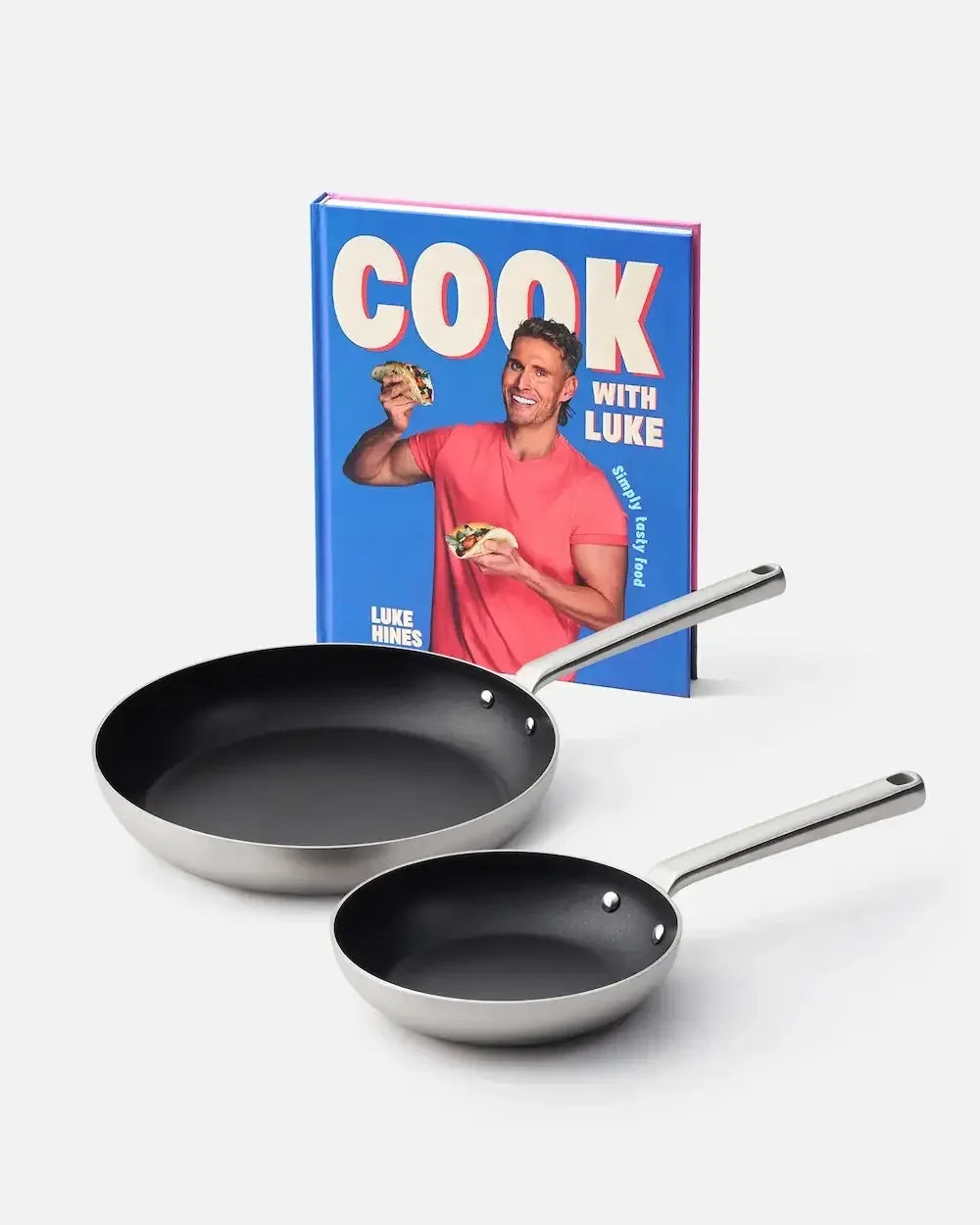 Two nonstick frying pans with stainless steel handles in front of a blue cookbook.
