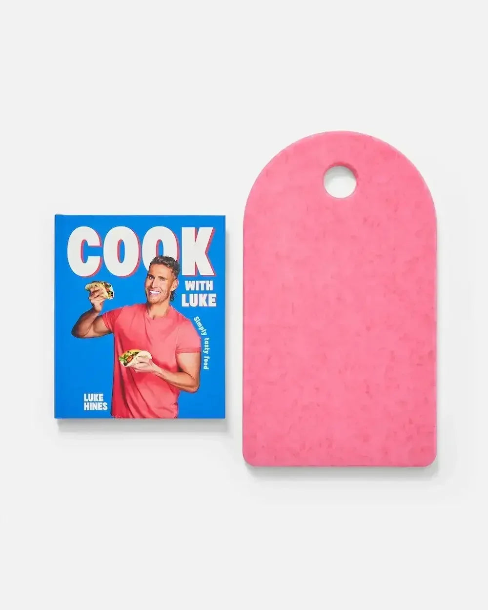 Blue cookbook with smiling man holding food next to a pink cutting board on white background