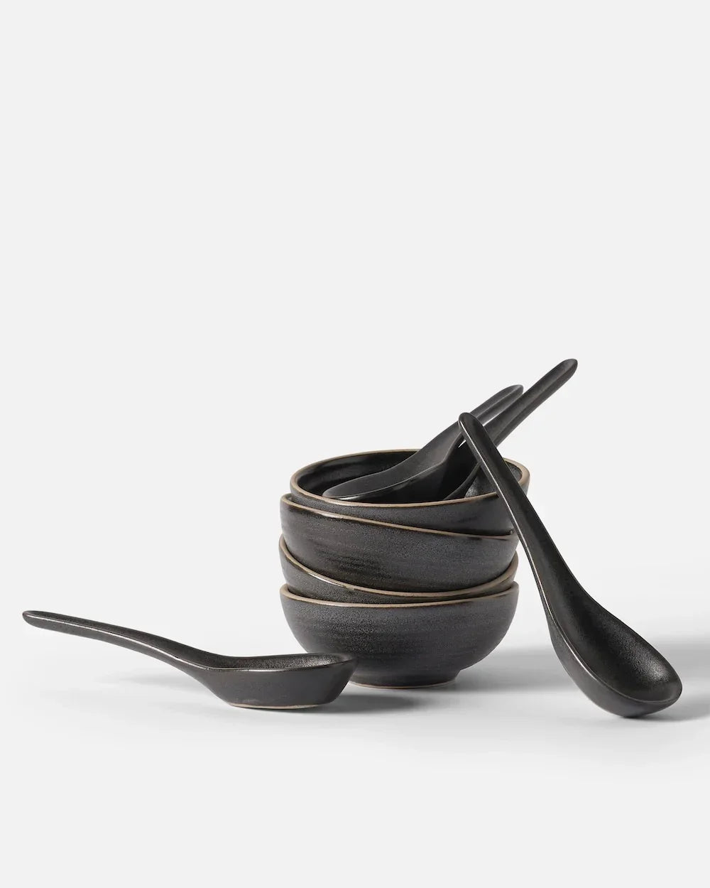 Stack of three black ceramic bowls with matching spoons on white background Asoke by Marion Grasby