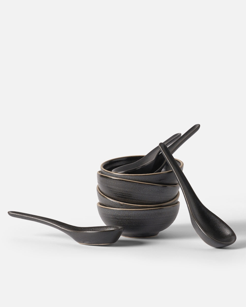 Stacked matte black ceramic bowls with matching soup spoons on a white background