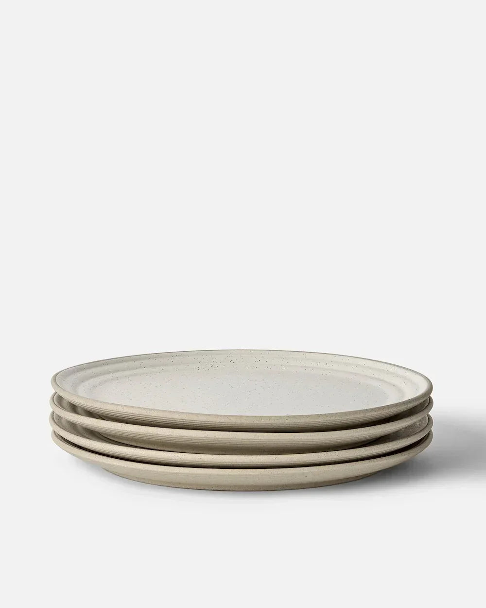 Stack of four minimalist beige ceramic dinner plates with subtle speckled texture