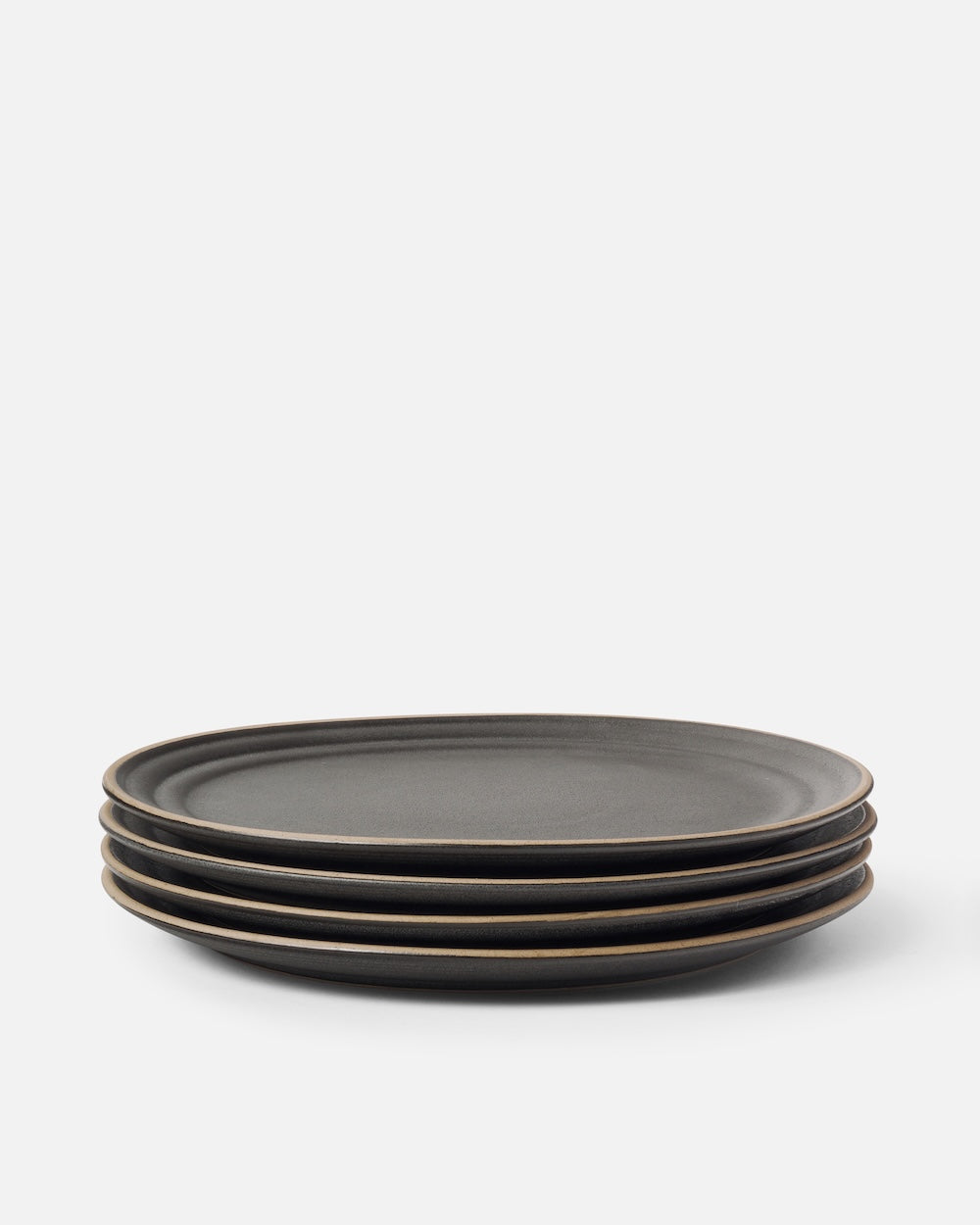 Stack of four matte charcoal ceramic dinner plates on a plain white background