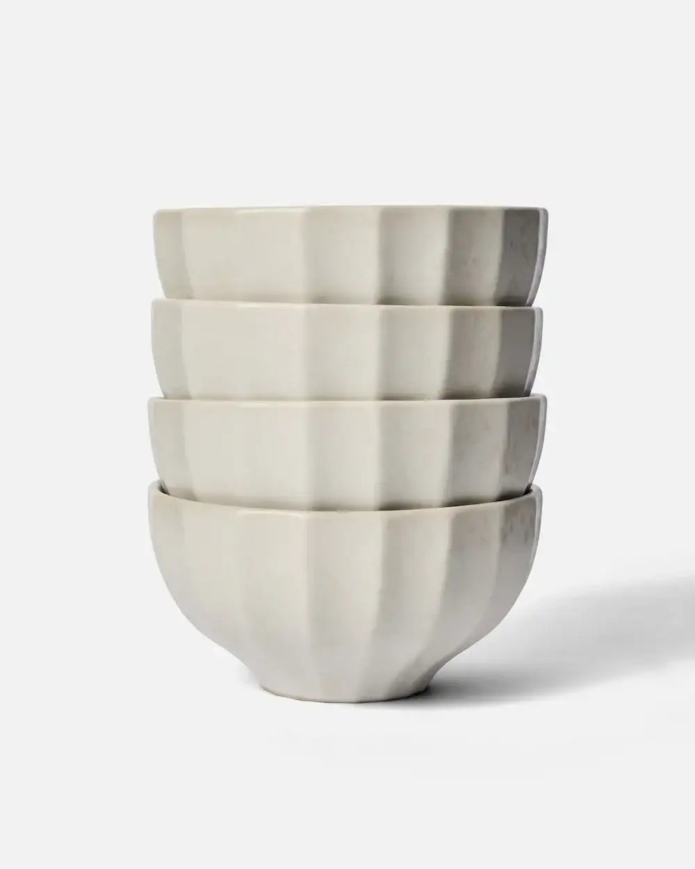 Stack of four white fluted ceramic cereal bowls on white background by Marion Grasby