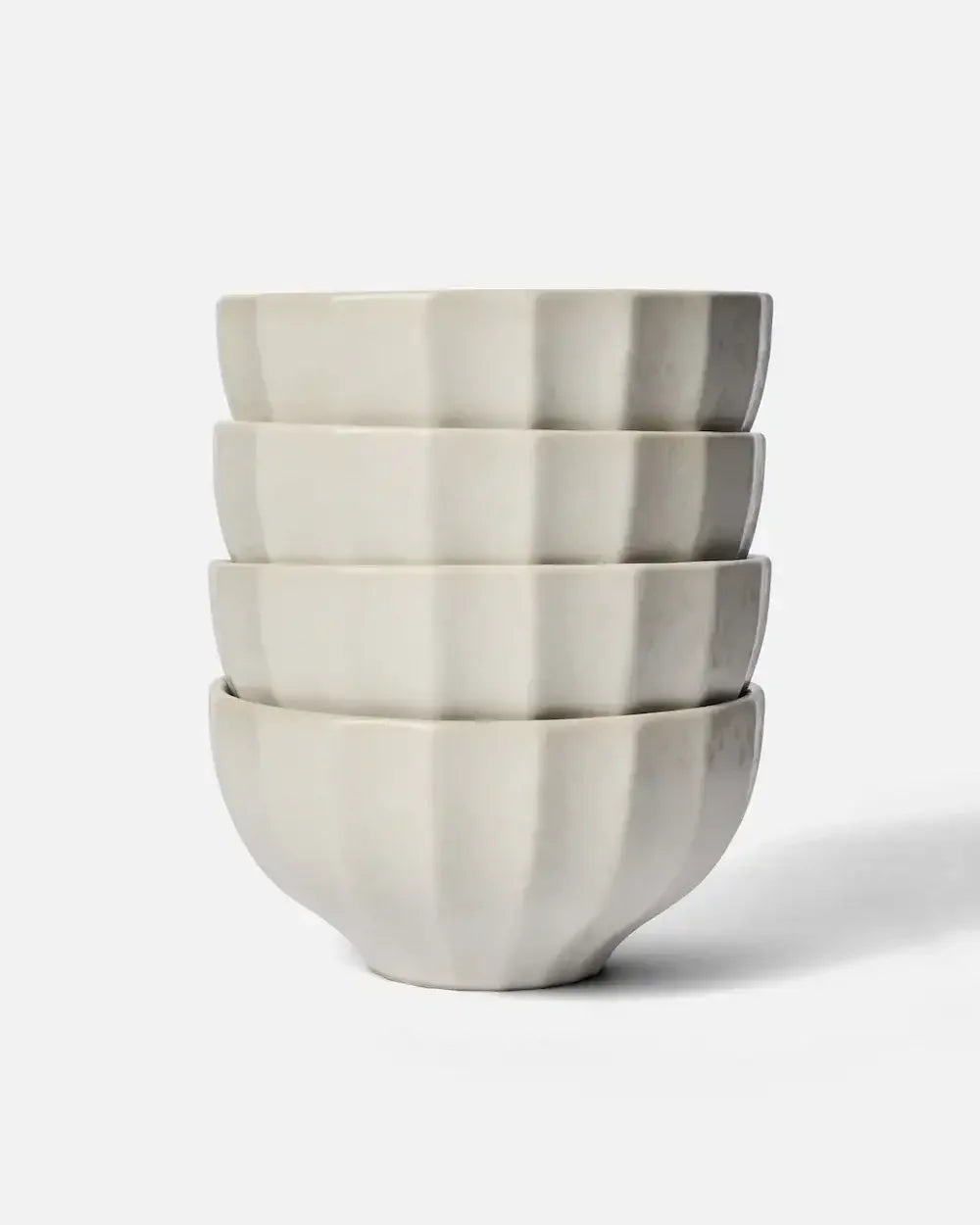 Stack of four white fluted ceramic cereal bowls on a plain background