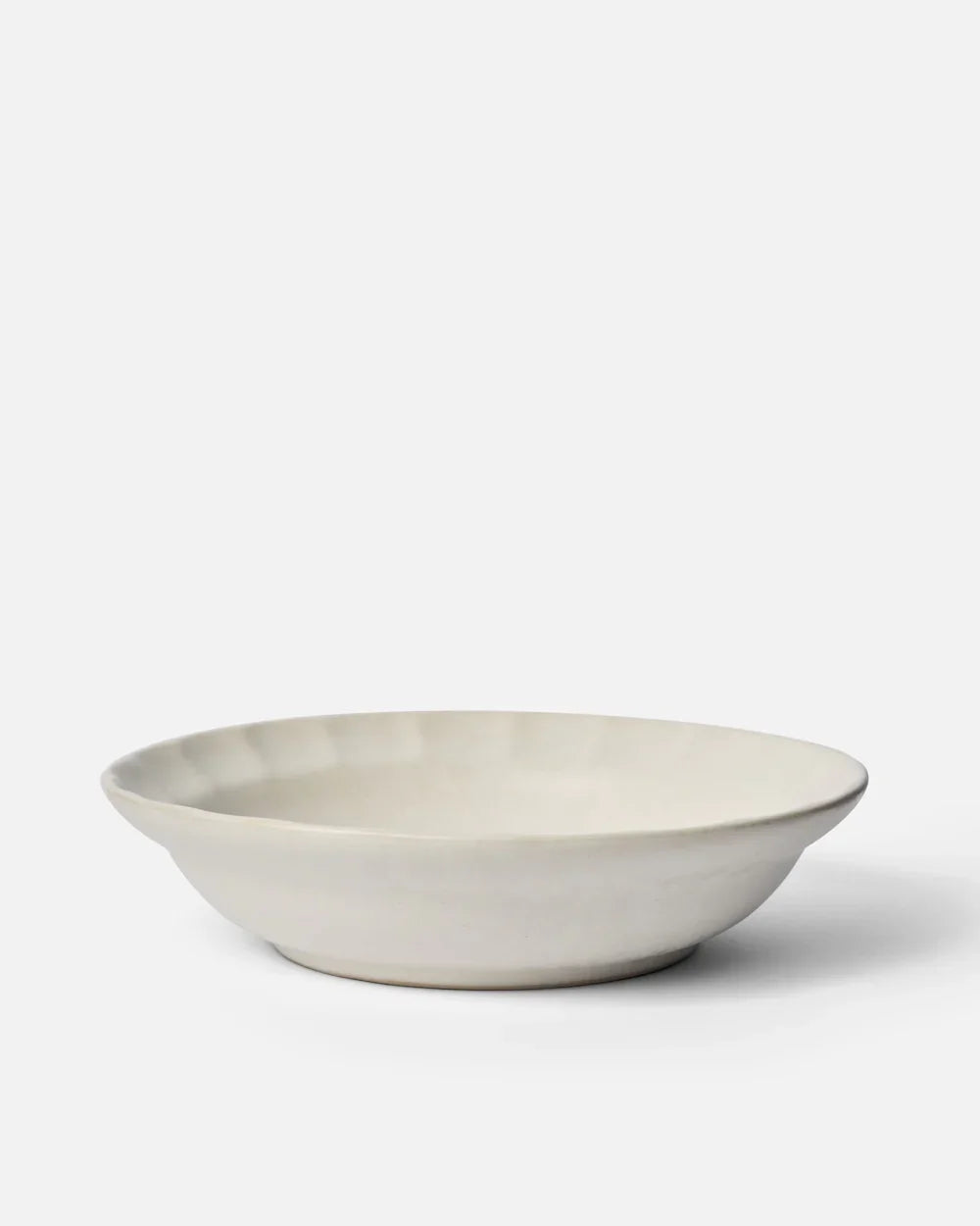 Off-white ceramic pasta bowl with fluted rim on plain white background by Marion Grasby