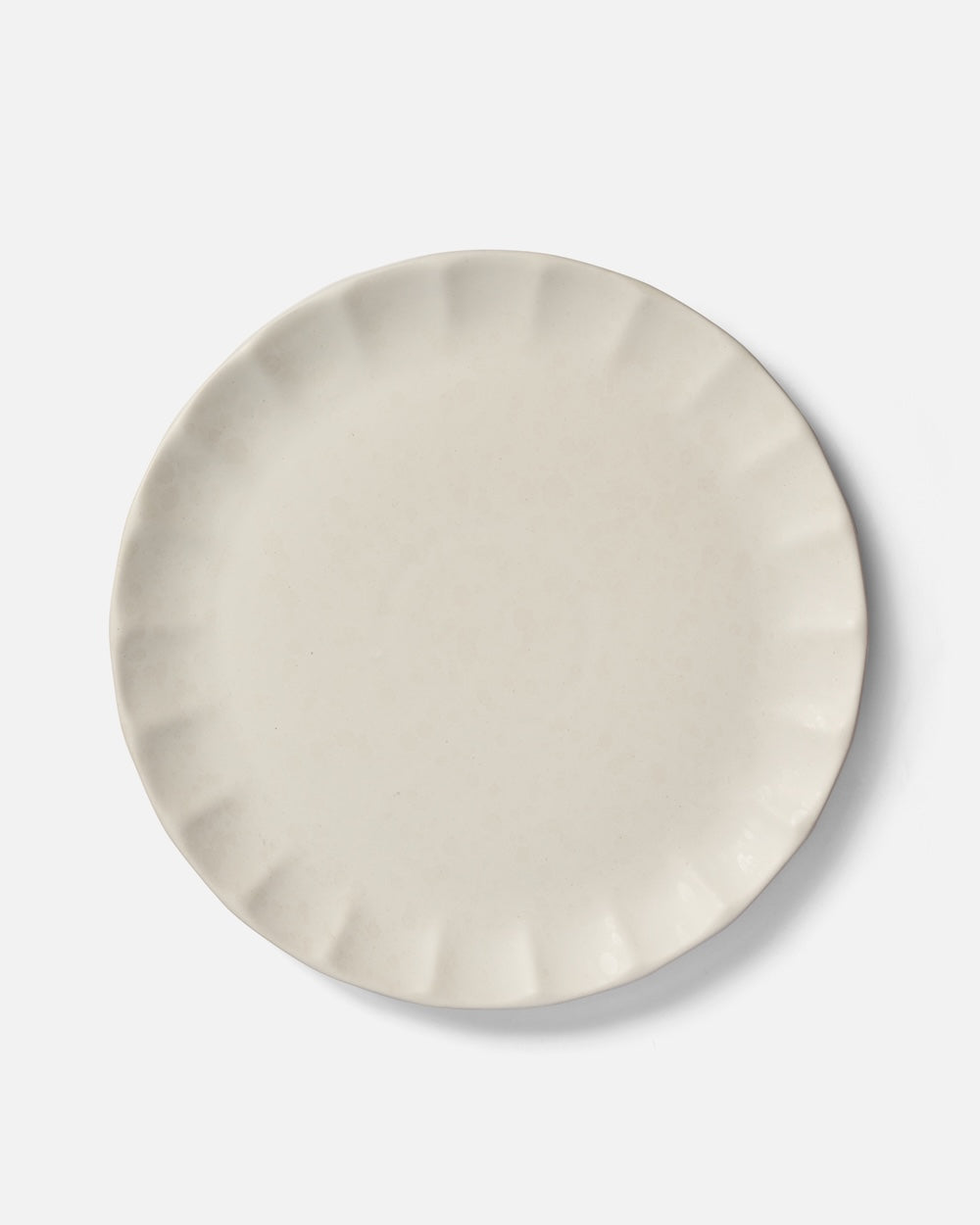 Beige ceramic dinner plate with fluted edge on white background