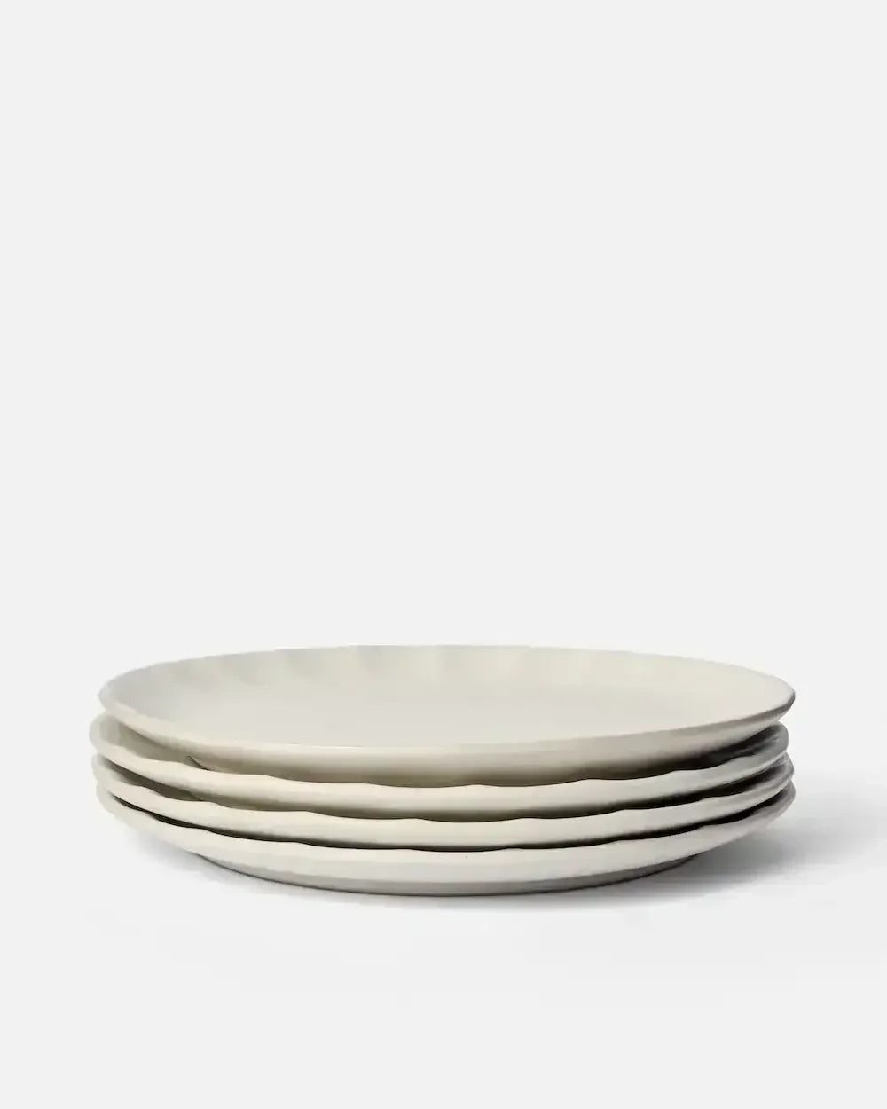 Set of four white ceramic dinner plates with wavy edges on a plain background