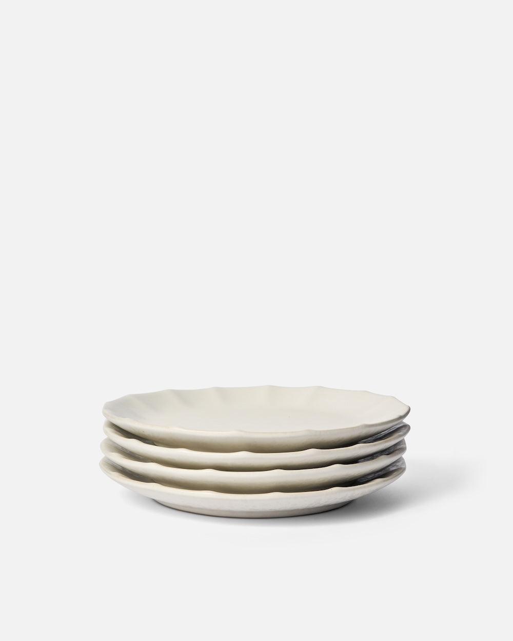 Stack of four white ceramic side plates with wavy edges on a plain background