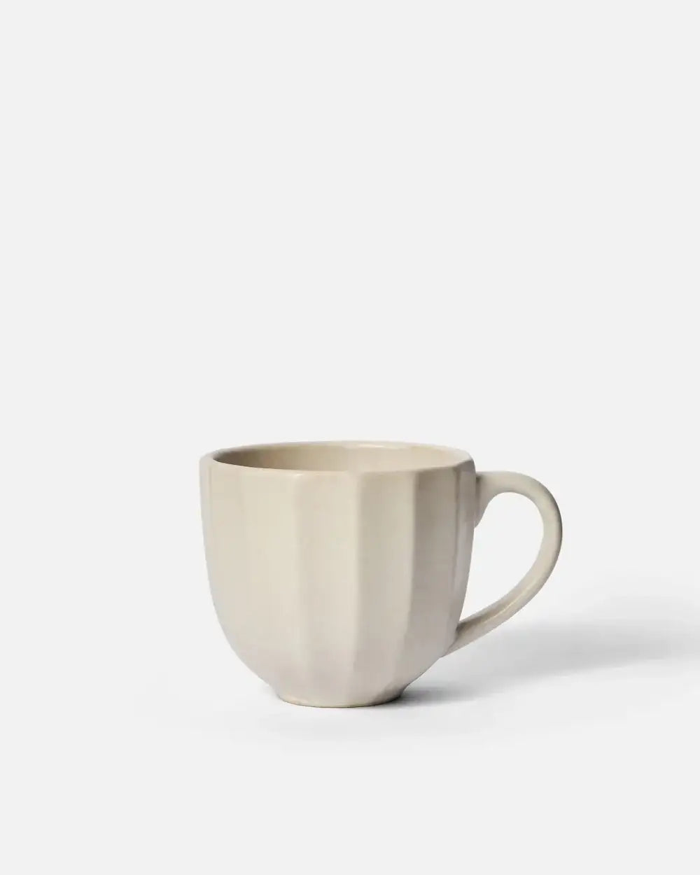 Cream-colored ceramic mug with ribbed texture and handle, minimalist design on white background