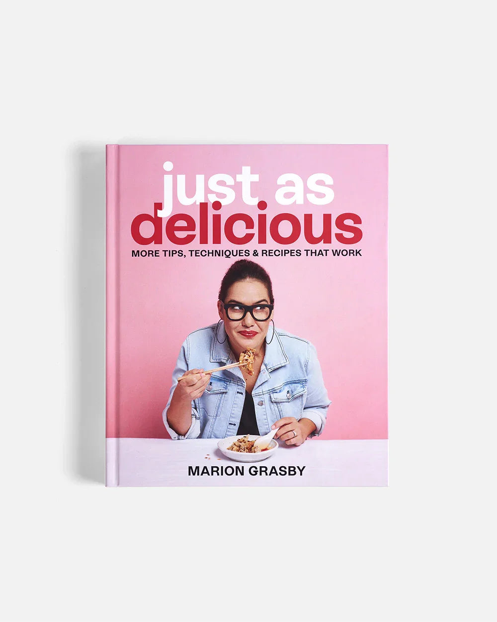 Cookbook Just As Delicious by Marion Grasby with a photo of her eating food with chopsticks on pink background
