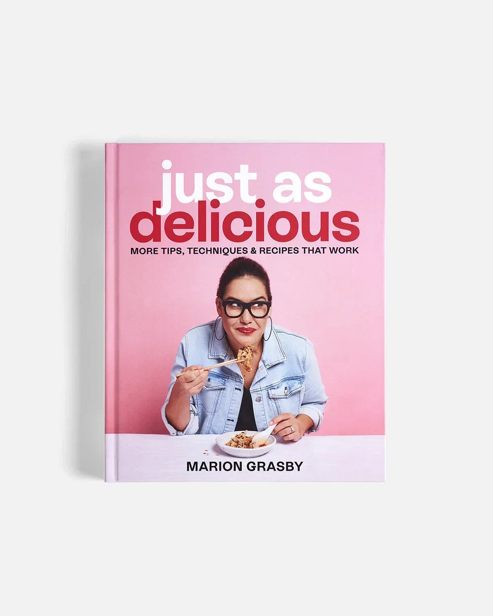 Cookbook Just As Delicious by Marion Grasby with a photo of her eating food with chopsticks on pink background