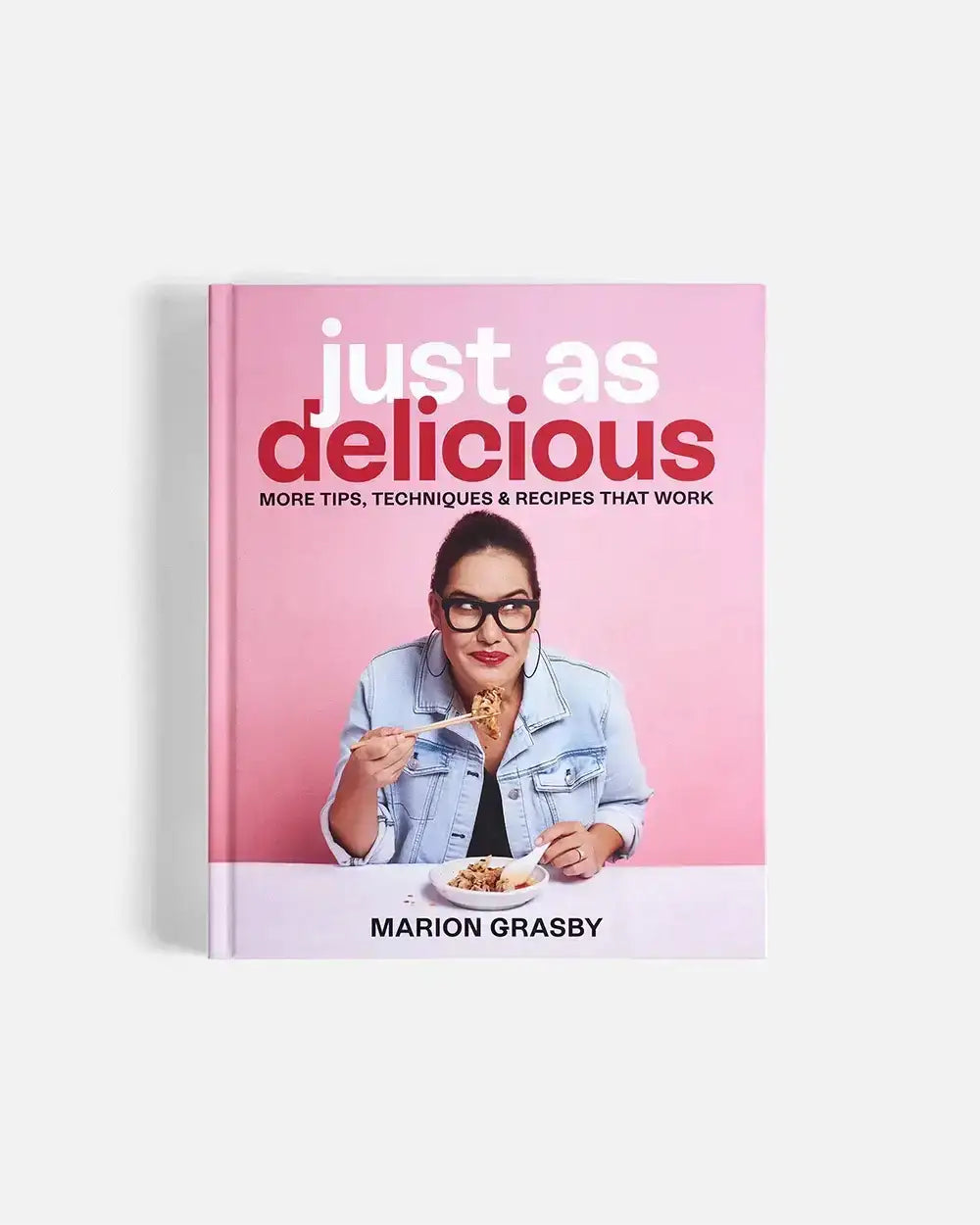 Cookbook Just As Delicious by Marion Grasby with a photo of her eating food with chopsticks on pink background
