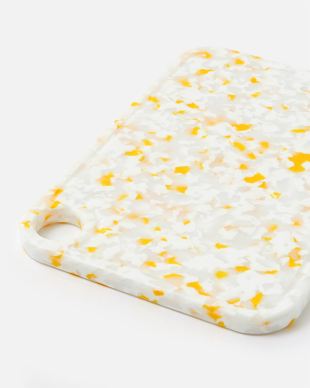 White and yellow terrazzo cutting board with rounded corner and handle hole on white background