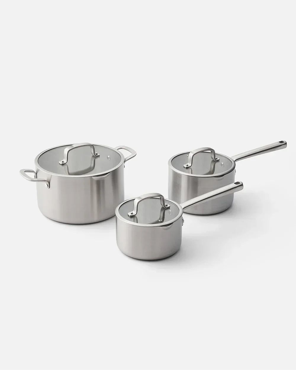 Three-piece stainless steel saucepan set with glass lids on white background