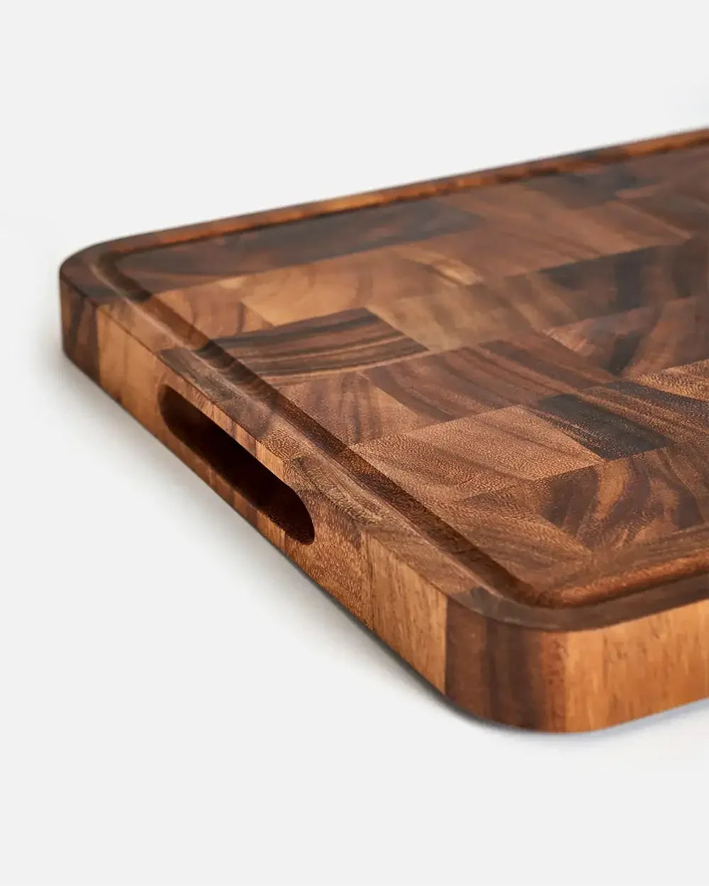 Close-up of a wooden end-grain chopping board with juice groove and hand slot