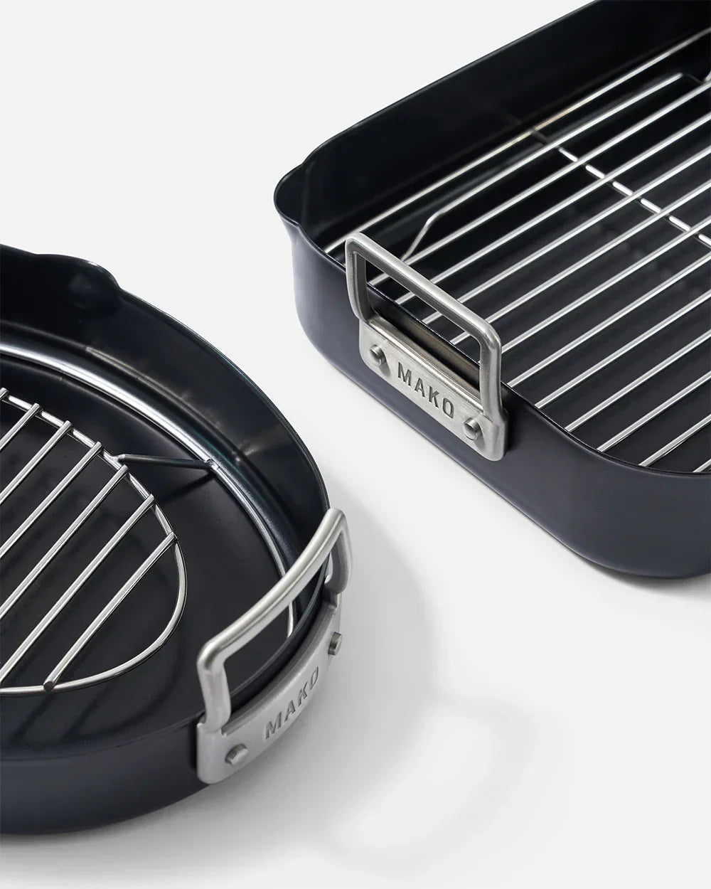 Two black MAKO roasting pans with stainless steel handles and wire racks on white background