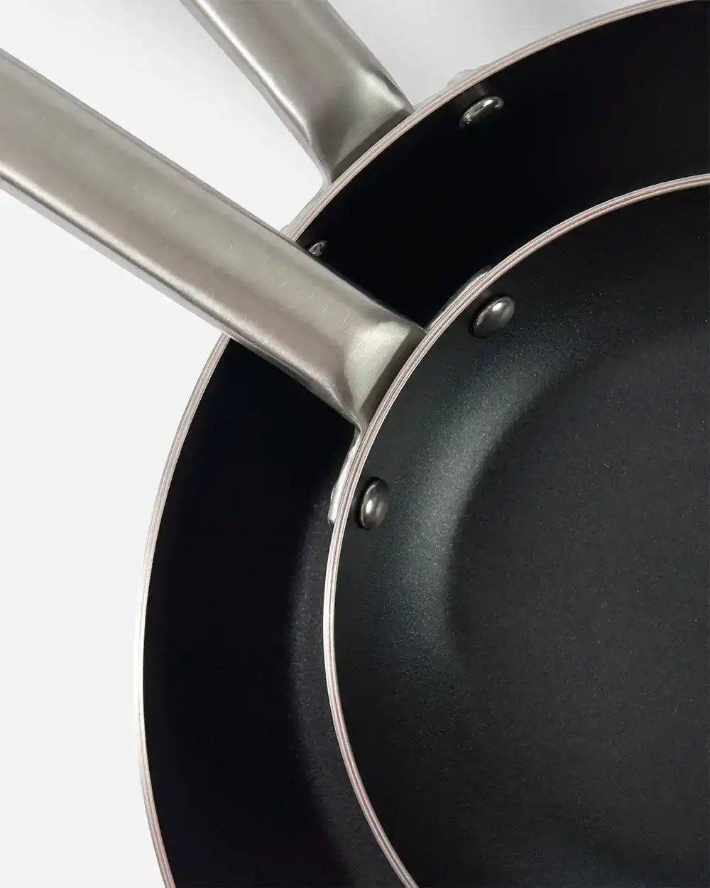 Close-up of two stacked Mako non-stick frying pans with stainless steel handles on white background