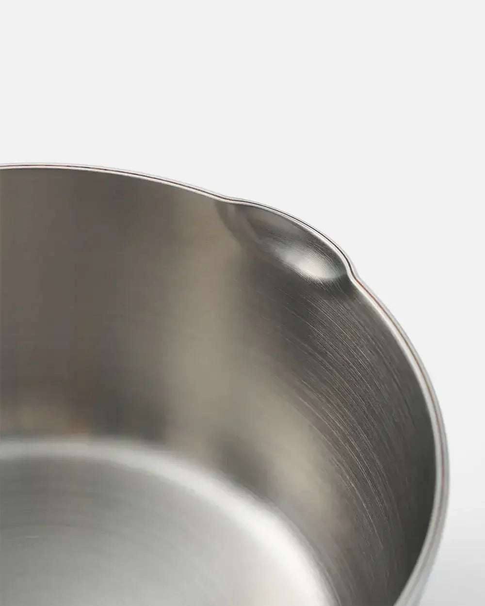 Close-up of a stainless steel cookware rim with a pouring spout on white background