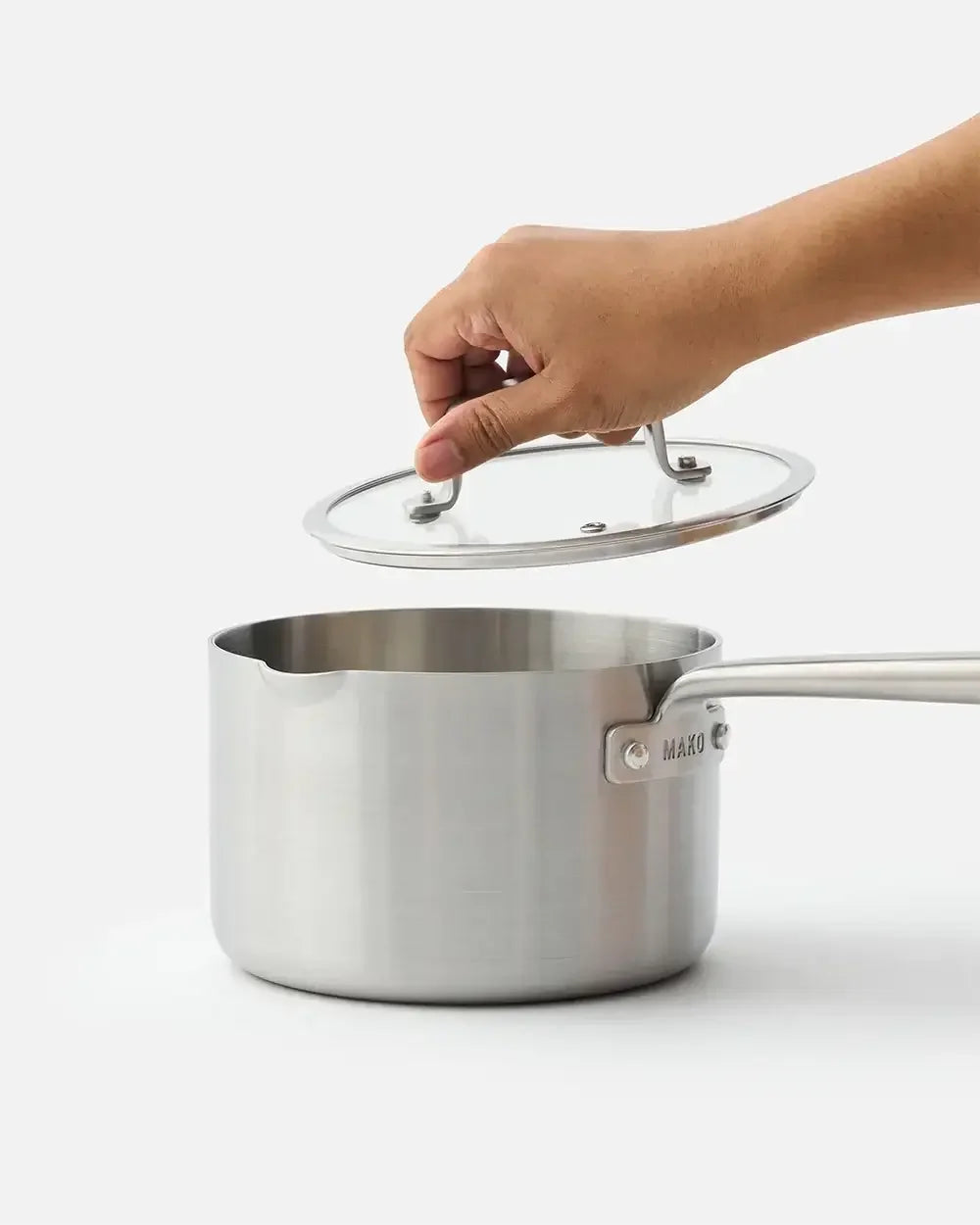 Hand lifting lid off stainless steel saucepan with long handle on white background