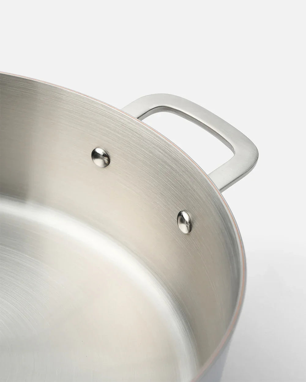 Close-up of brushed stainless steel cookware handle with riveted construction by Marion Grasby