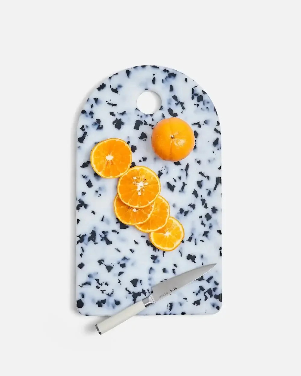 Speckled terrazzo cutting board with sliced orange and white-handled kitchen knife