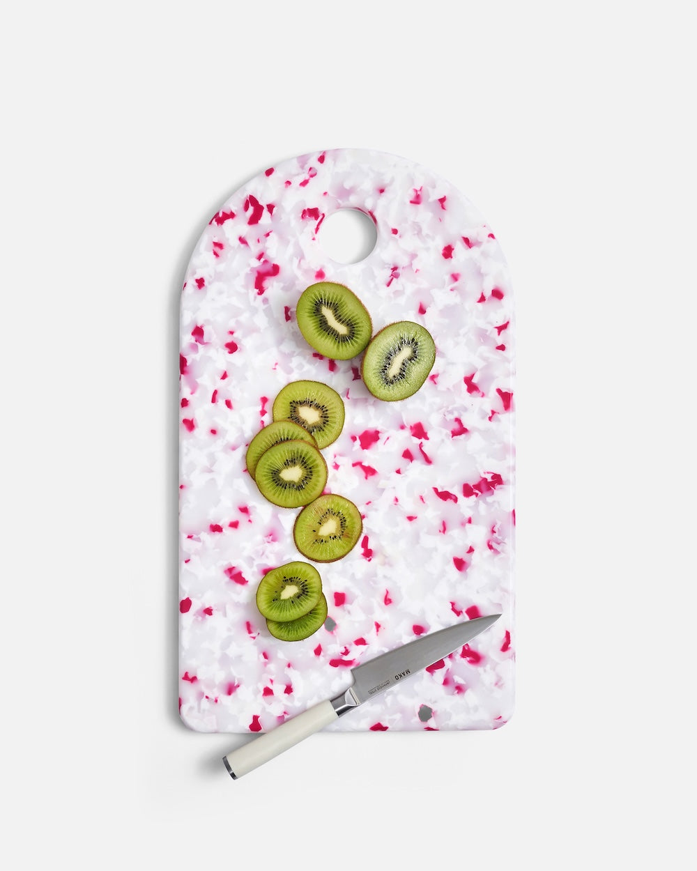 Terrazzo cutting board with pink accents, sliced kiwi, and kitchen knife on white background