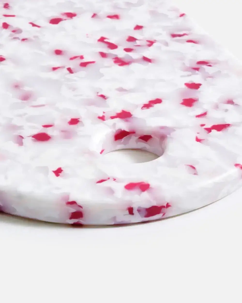 Close-up of a white and red speckled kitchen cutting board with a round hole, designed by Marion Grasby