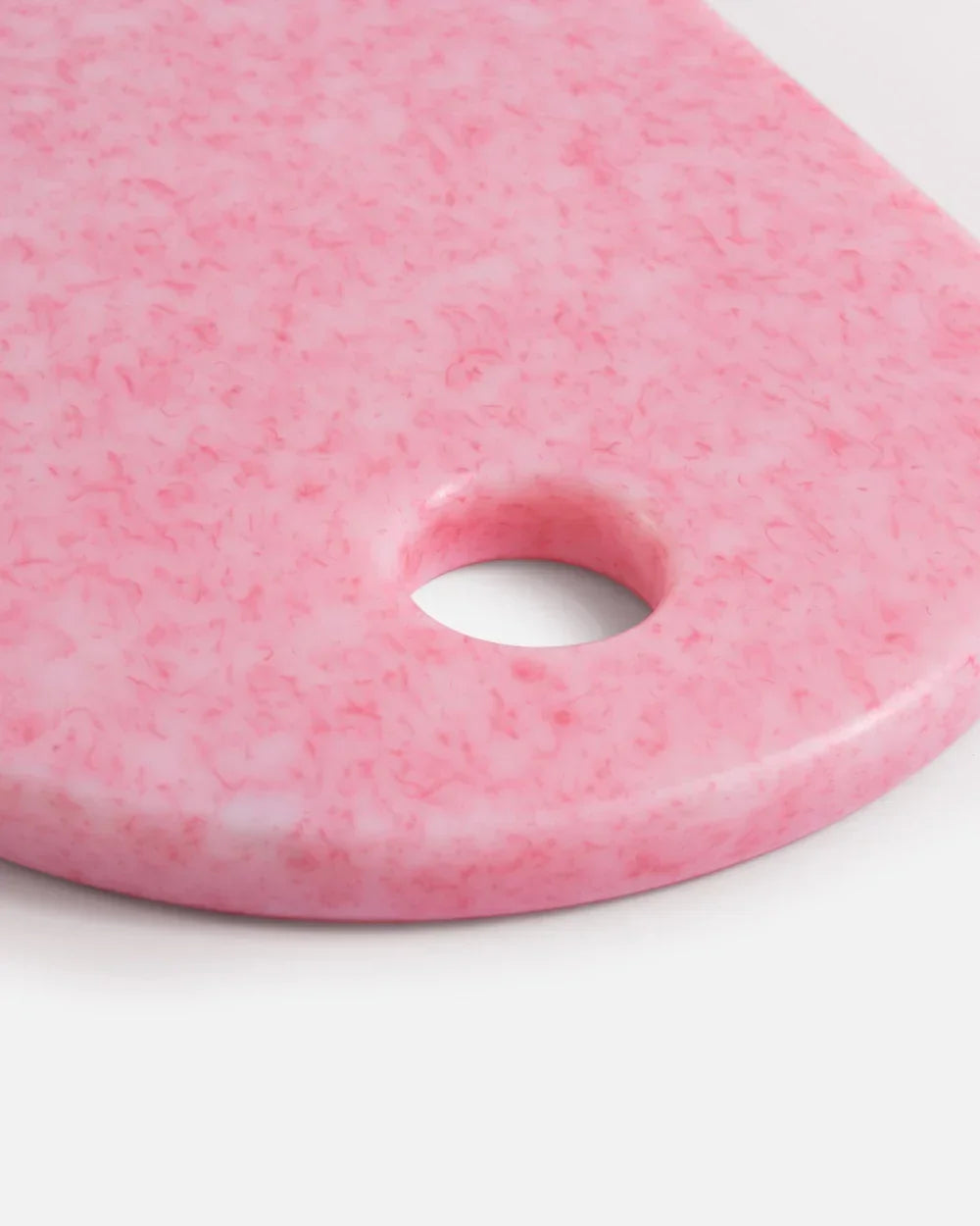 Pink marbled cutting board with rounded edges and a circular hole on a white background