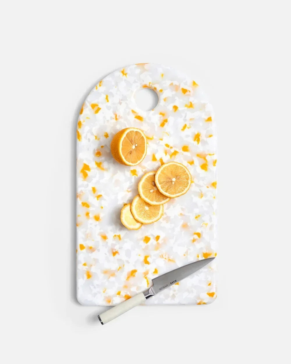 Sliced lemon on white and orange terrazzo cutting board with small kitchen knife