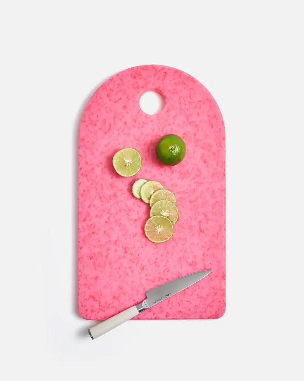 Pink cutting board with sliced lime, whole lime, and Mako knife by Marion Grasby
