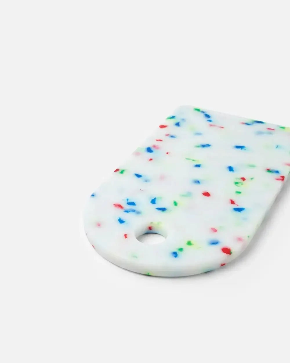White cutting board with colorful speckles and rounded corner on a plain background