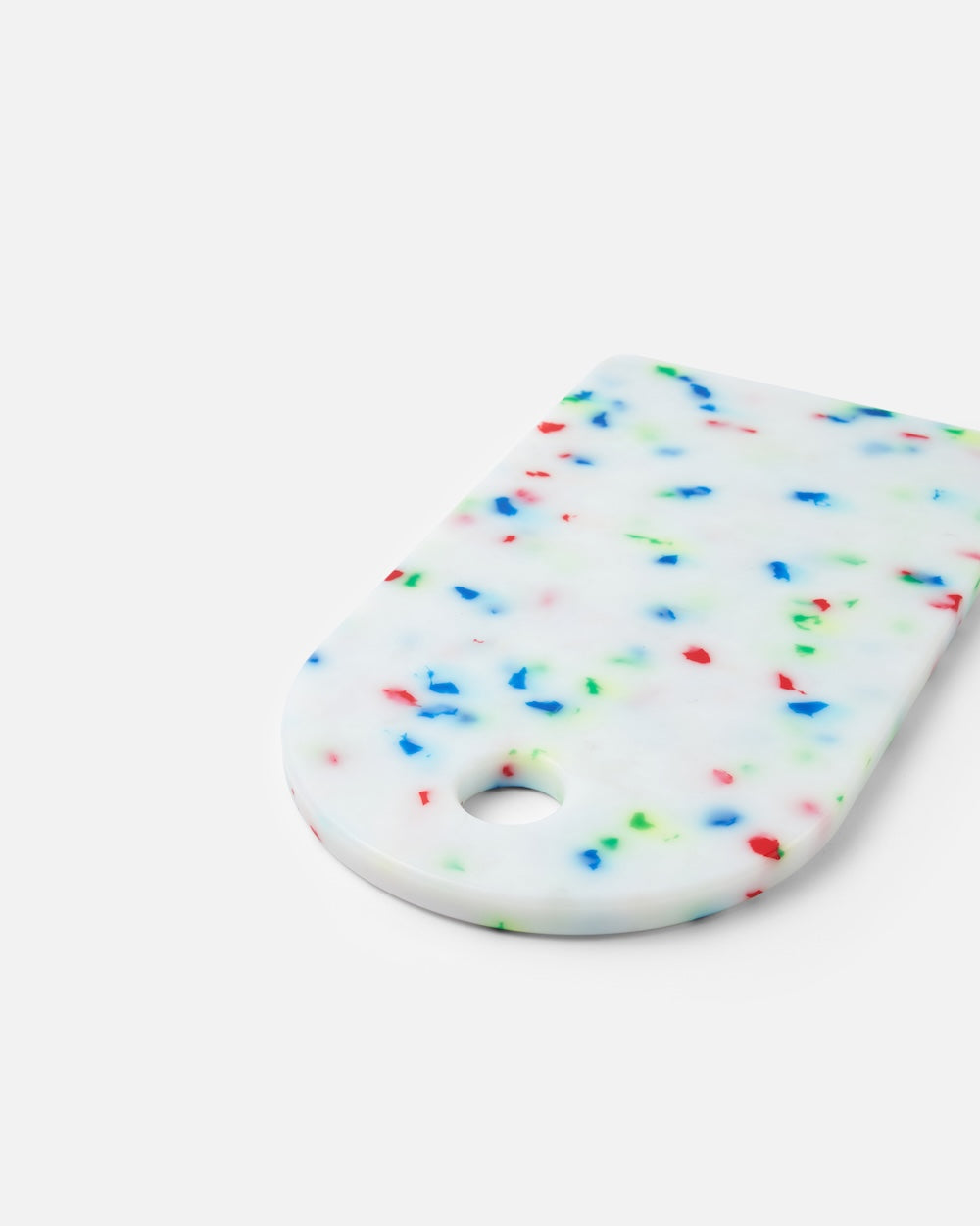 White cutting board with colorful speckles and rounded corner on a plain background