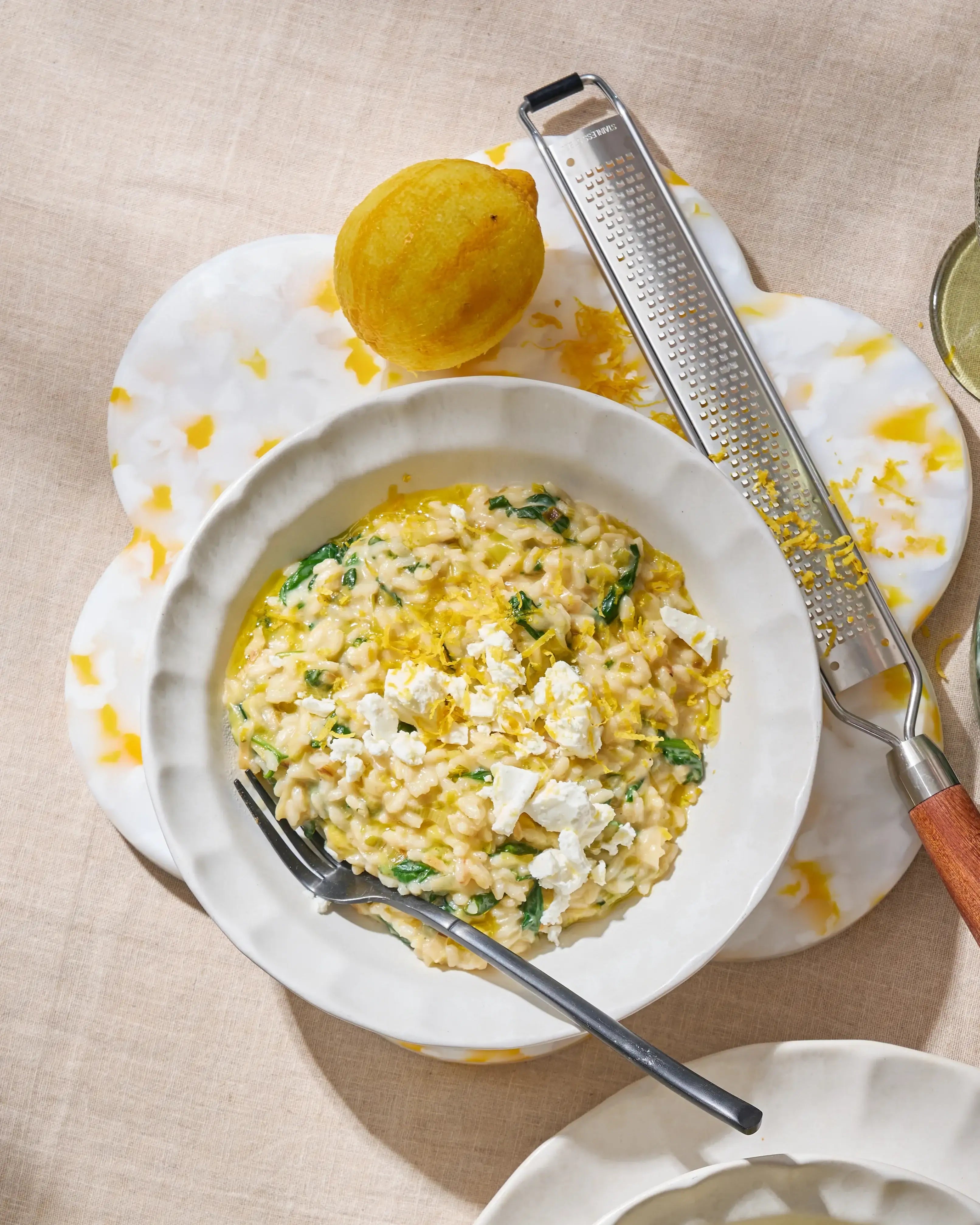 Creamy lemon risotto with spinach and feta in white bowl with lemon and zester on marble board