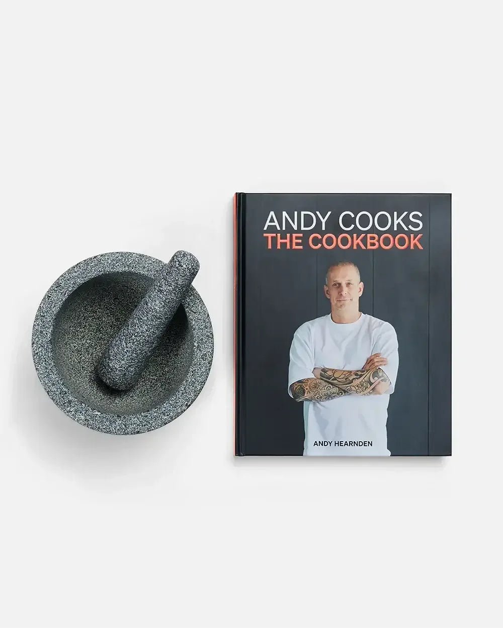 Granite mortar and pestle beside Andy Cooks cookbook on white background