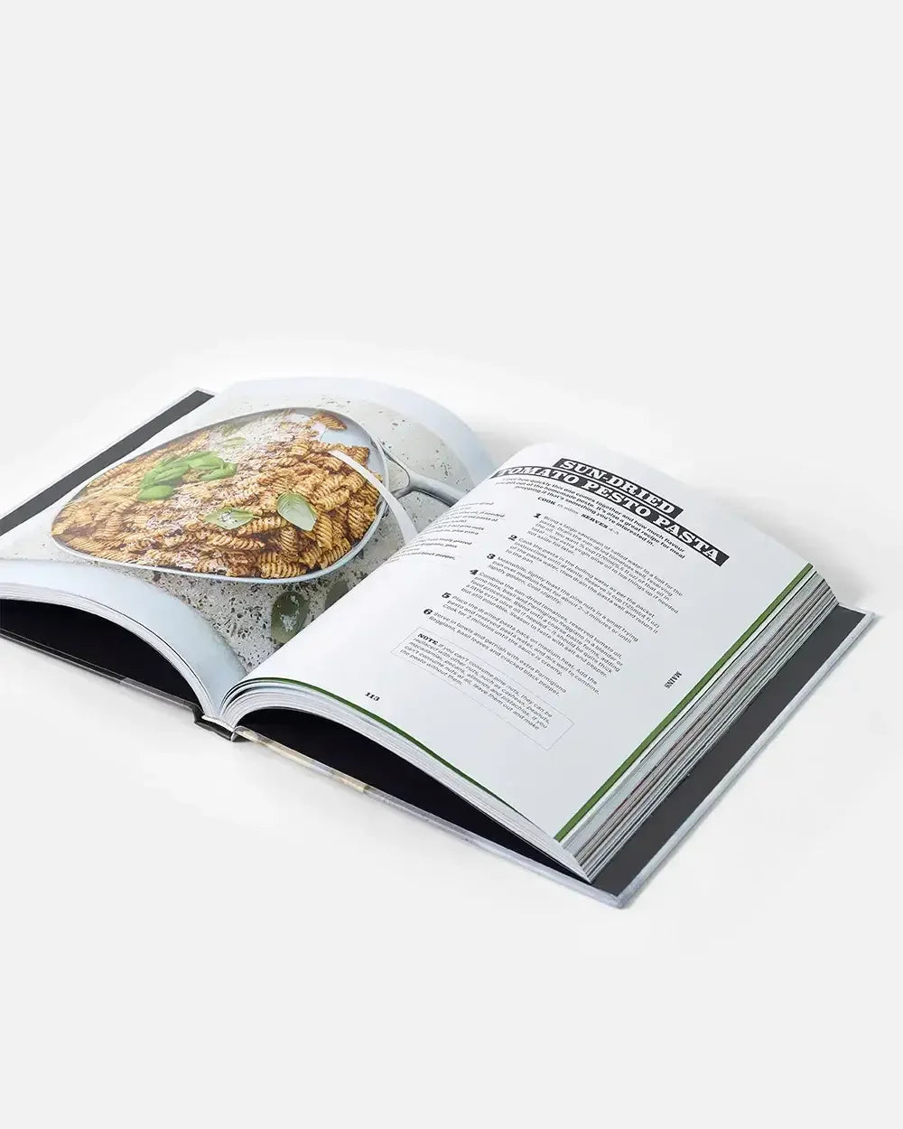 Open cookbook displaying a sun-dried tomato pesto pasta recipe with food photo.