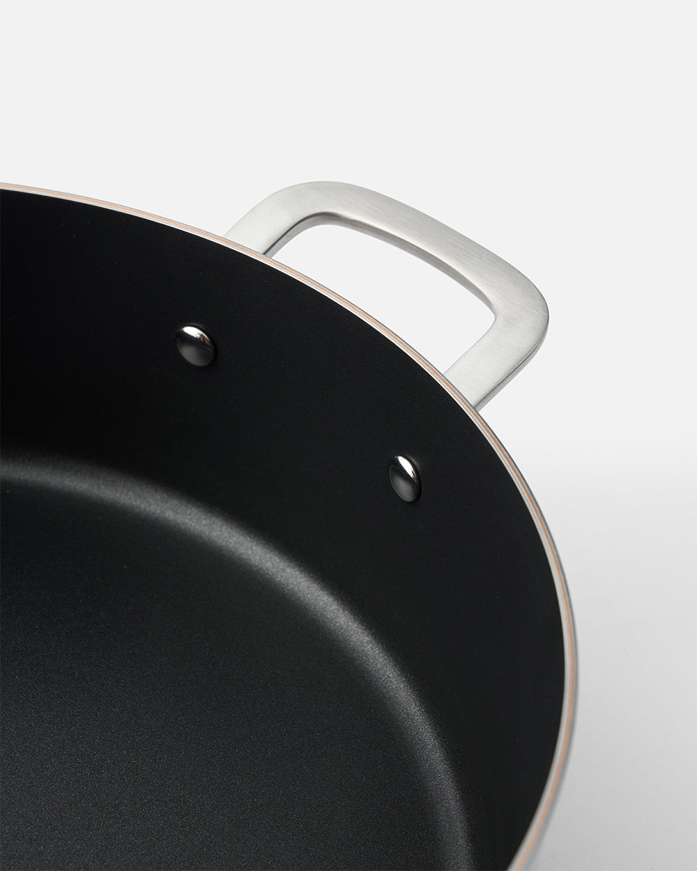 Close-up of a black nonstick essential pan with a metal handle on a white background