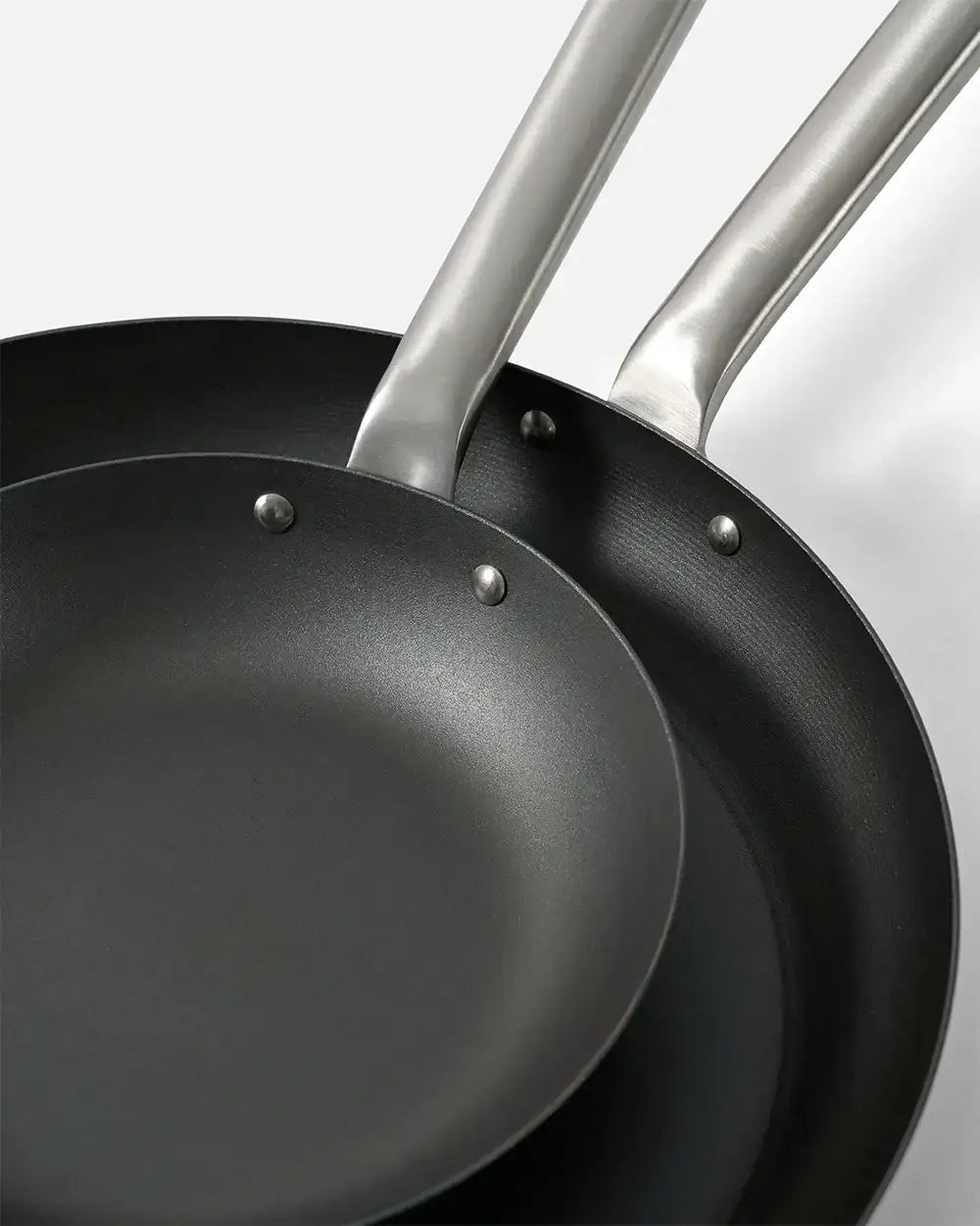 Close-up of two black non-stick frying pans with silver riveted handles on white background