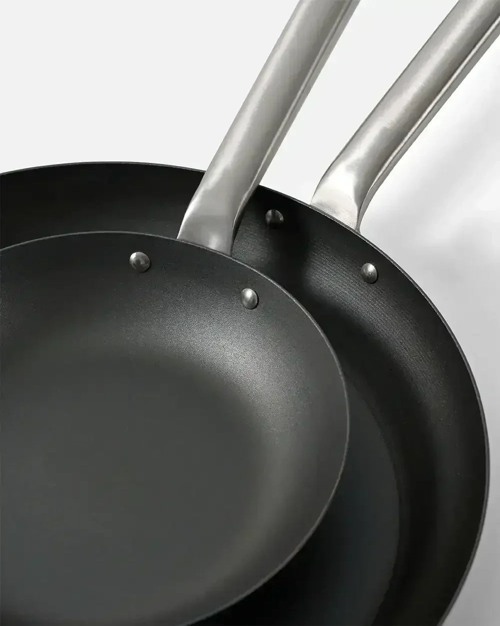 Two black steel frying pans with silver handles on a white background
