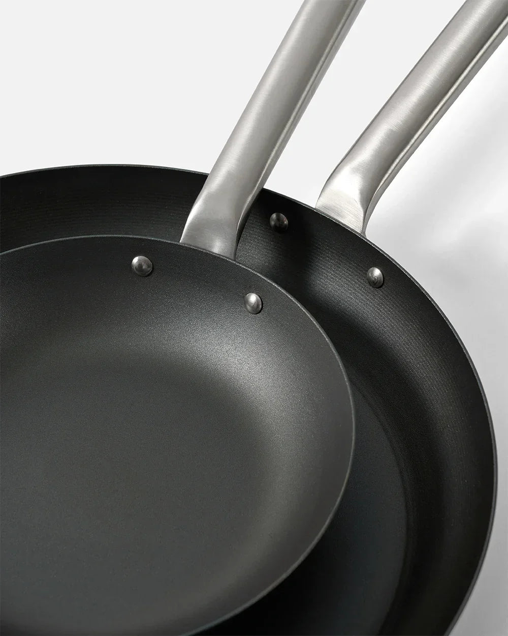 Close-up of two black non-stick frying pans with silver riveted handles on white background