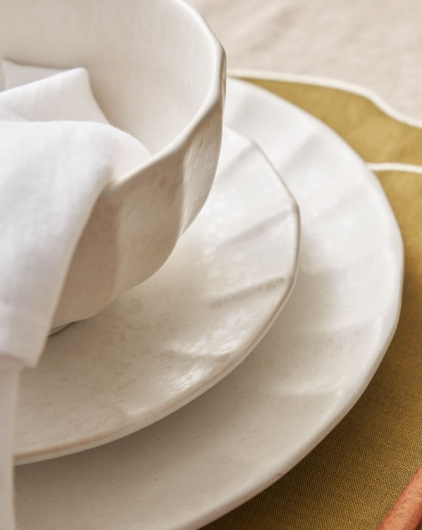 Stacked white ceramic bowl and plates with napkin on gold placemat, modern tableware setting