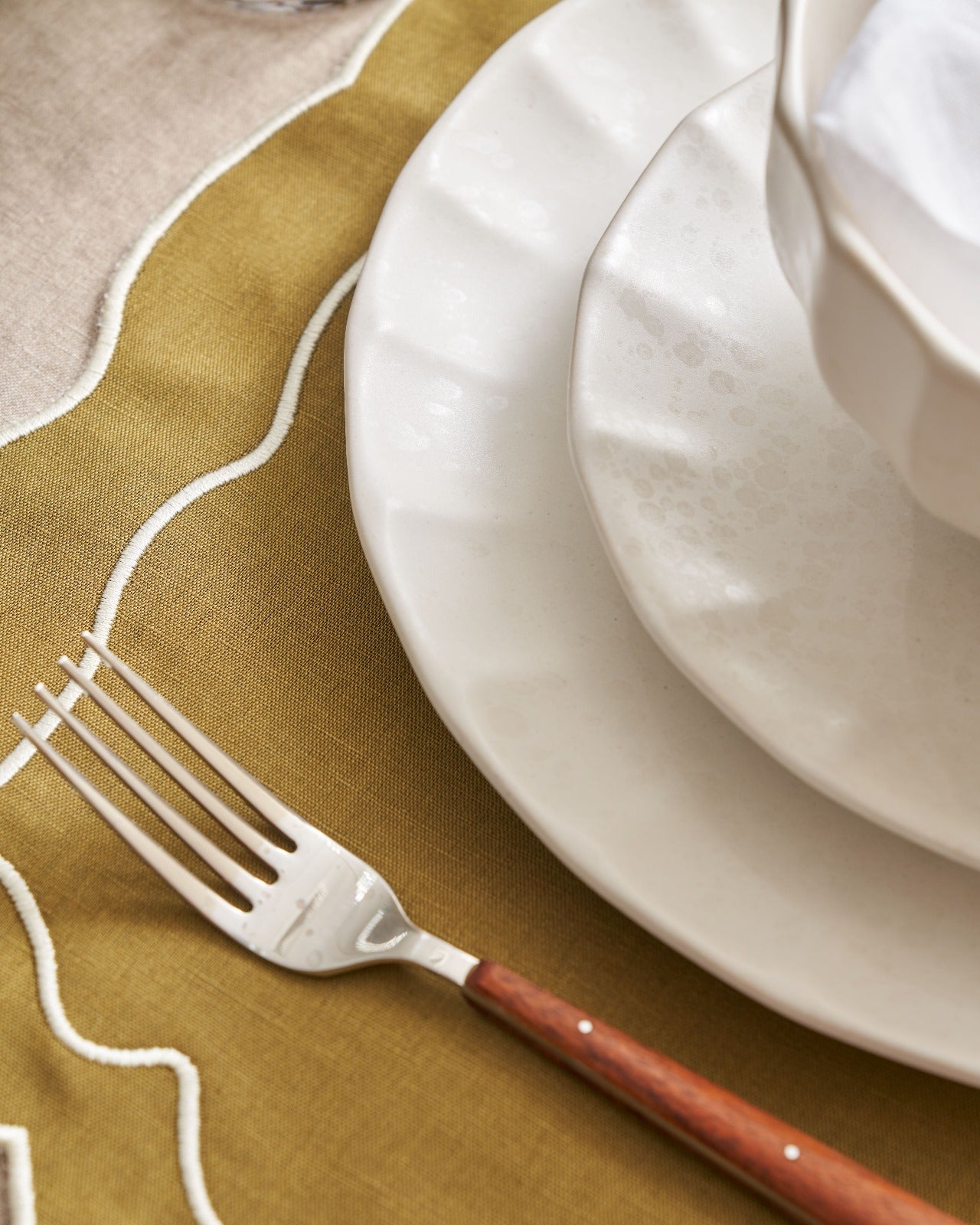 Ceramic dinnerware set with linen napkin and wood-handle fork on ochre tablecloth