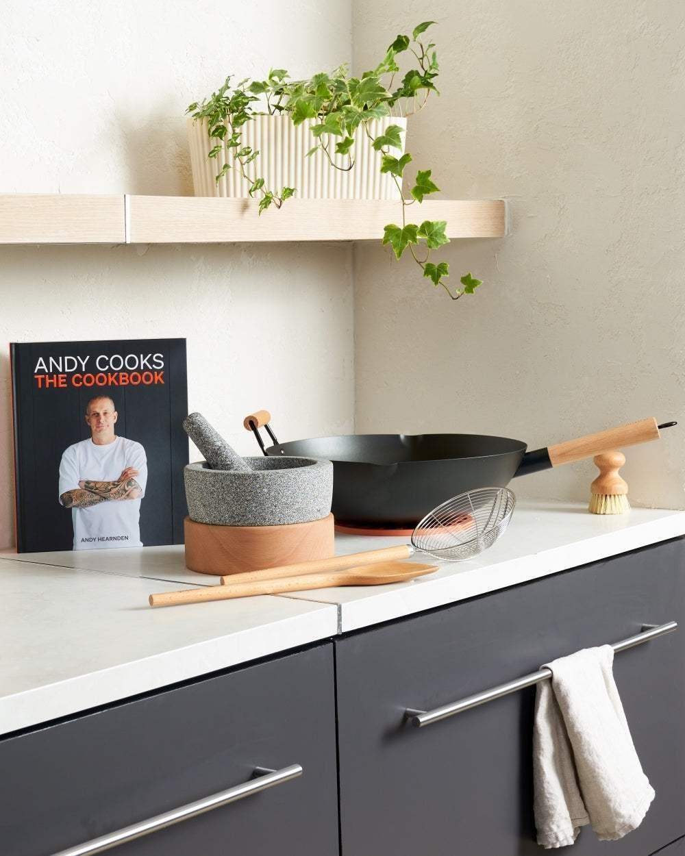 Modern kitchen with Andy Cooks cookbook, granite mortar and pestle, wok, and utensils on counter.