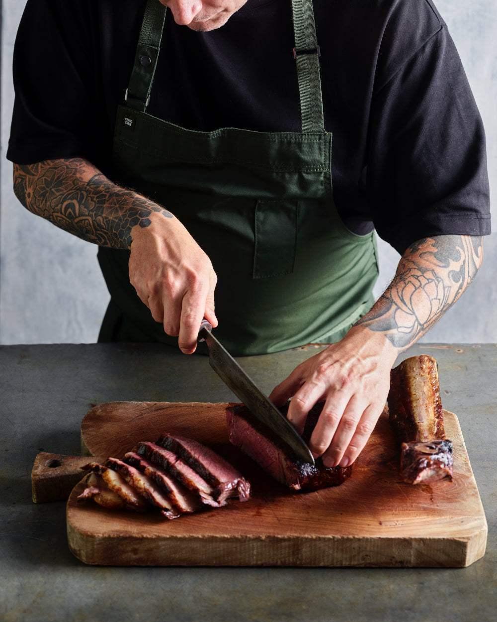 Chef in green apron slicing smoked beef brisket on wooden cutting board
