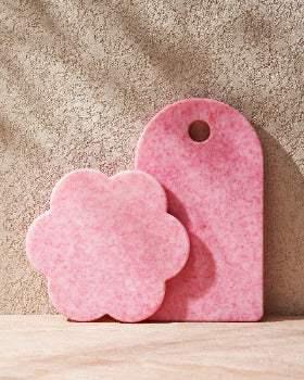 Pink recycled chopping boards, one flower-shaped and one rectangular, on a textured surface