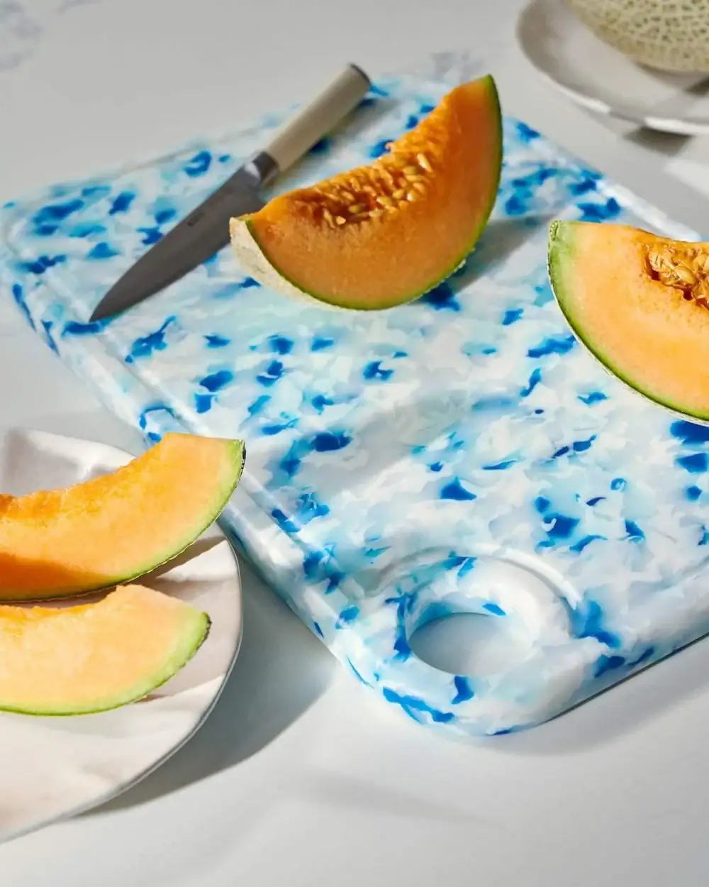 Blue recycled Asoke chopping board by Marion Grasby with sliced cantaloupe melon and knife