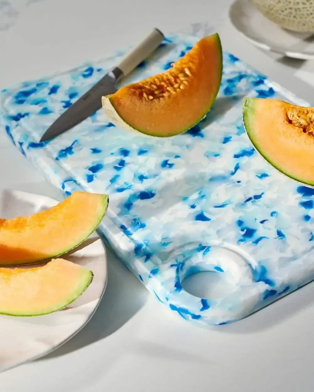 Blue and white recycled chopping board with knife and sliced melon on a kitchen counter