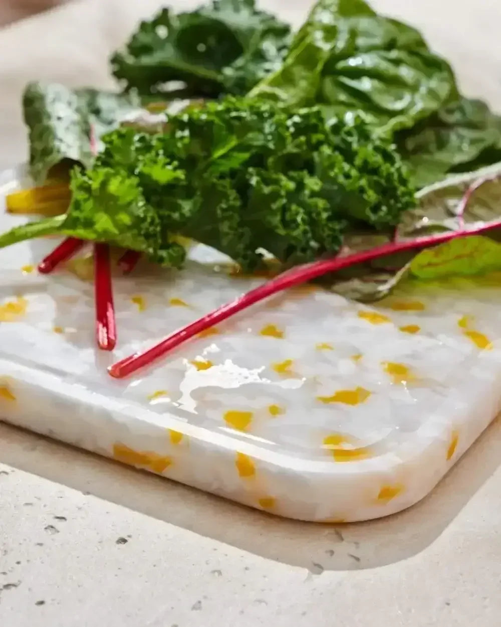 Recycled chopping board with yellow accents topped with fresh greens on a countertop